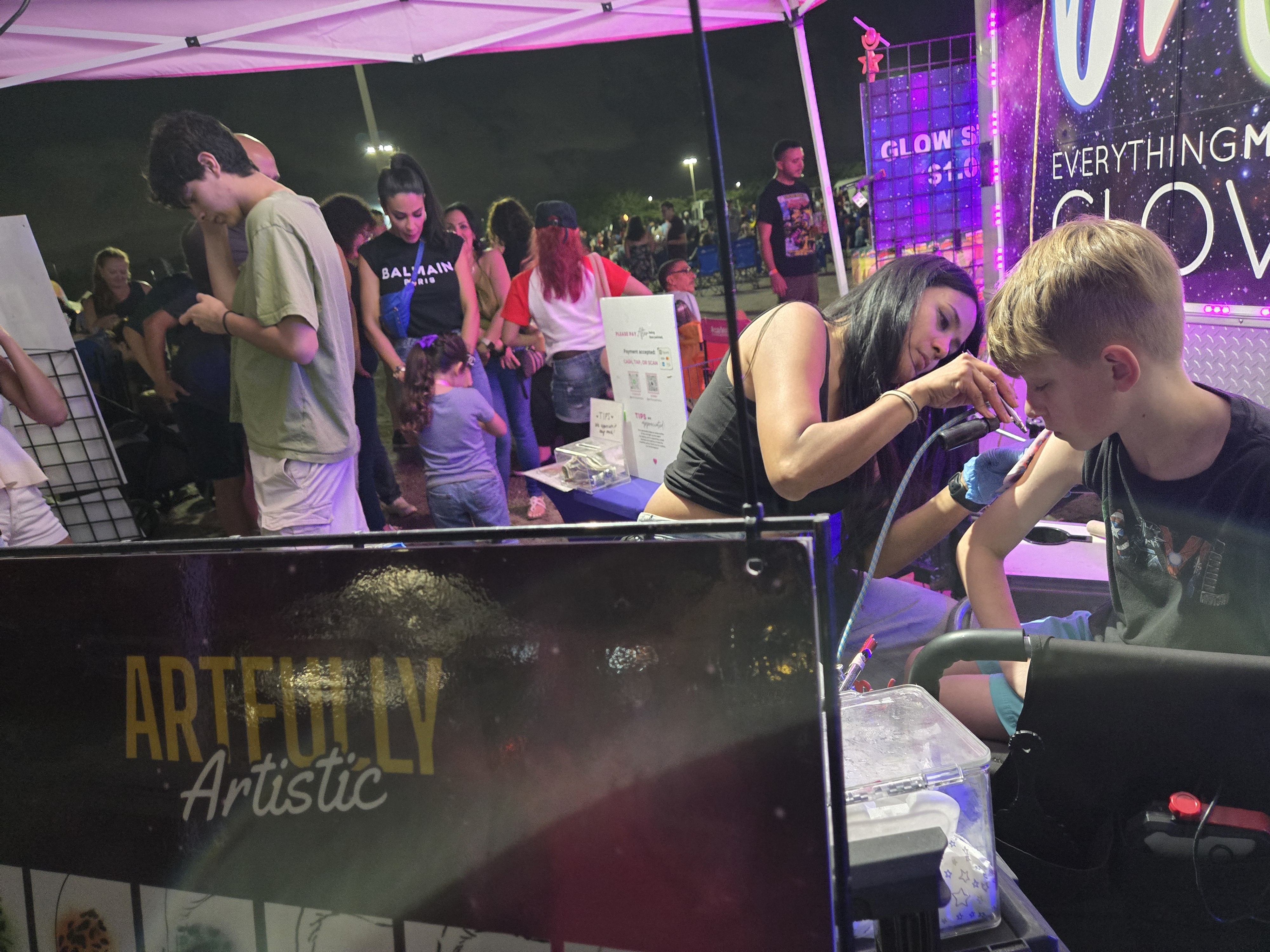 Artfully Artistic face painting station busy at night next to the EMG booth
