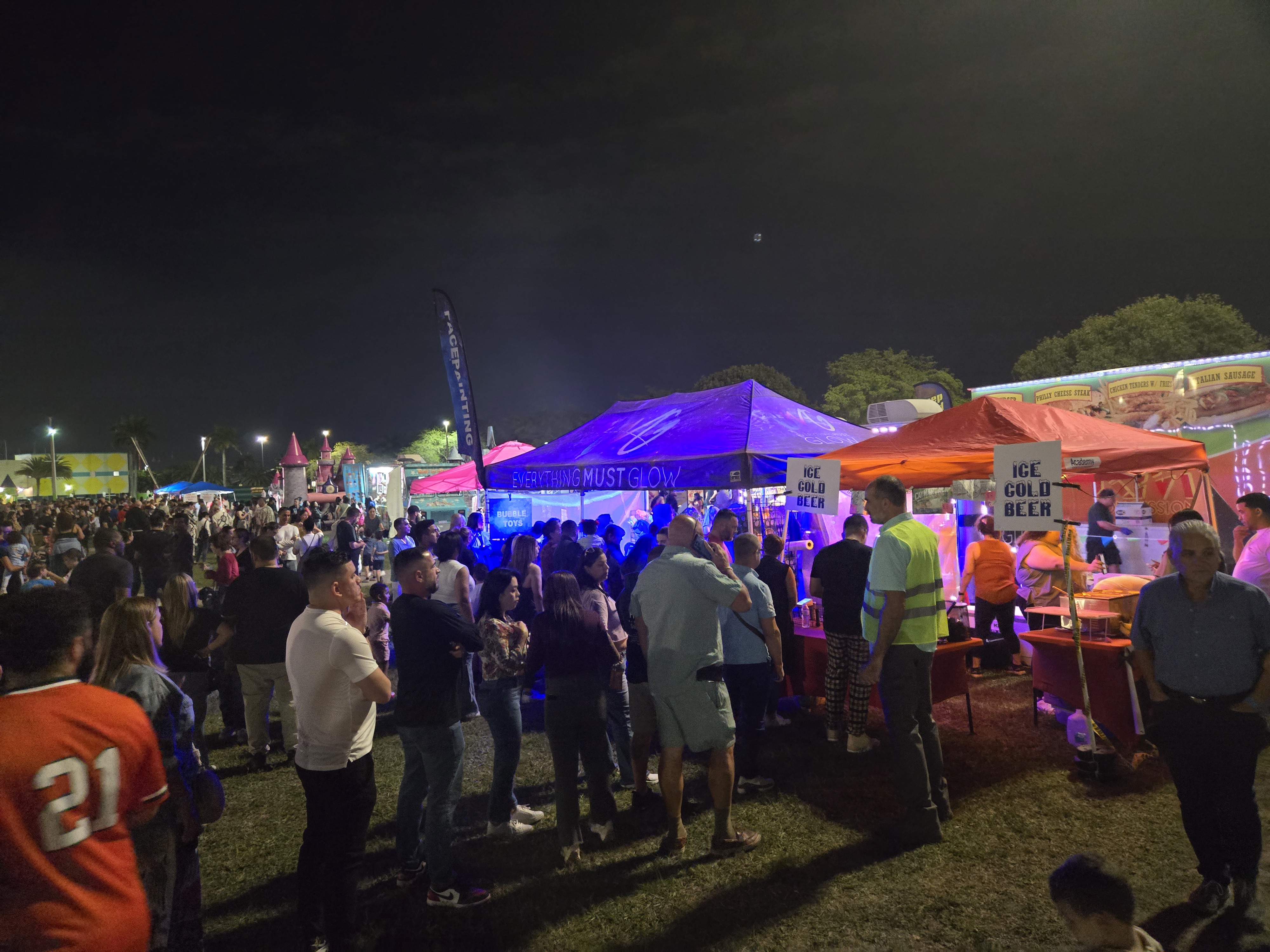 Massive crowd surrounding the Everything Must Glow booth on a busy festival night