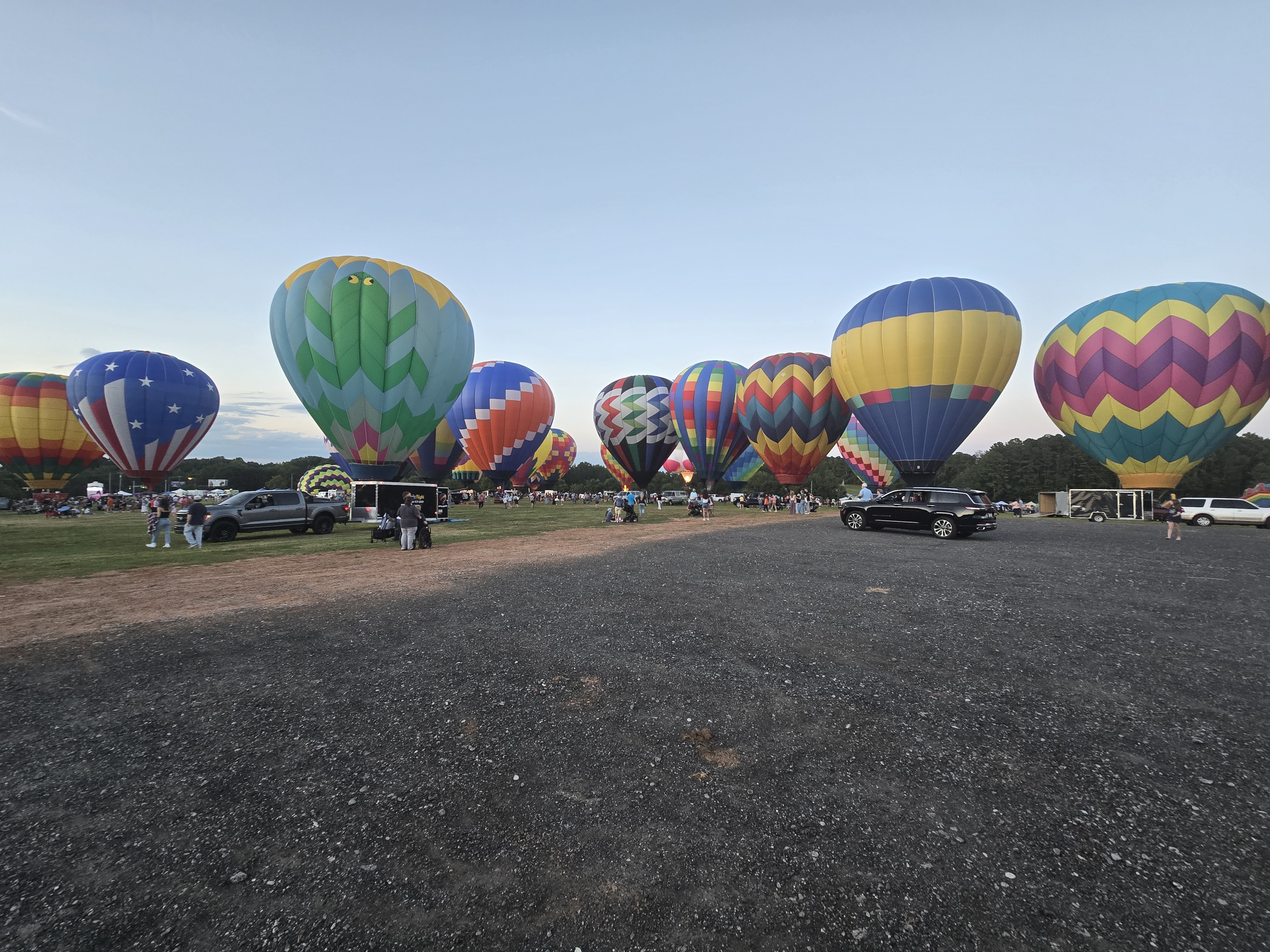 Colorful hot air balloons inflating across the field at sunset