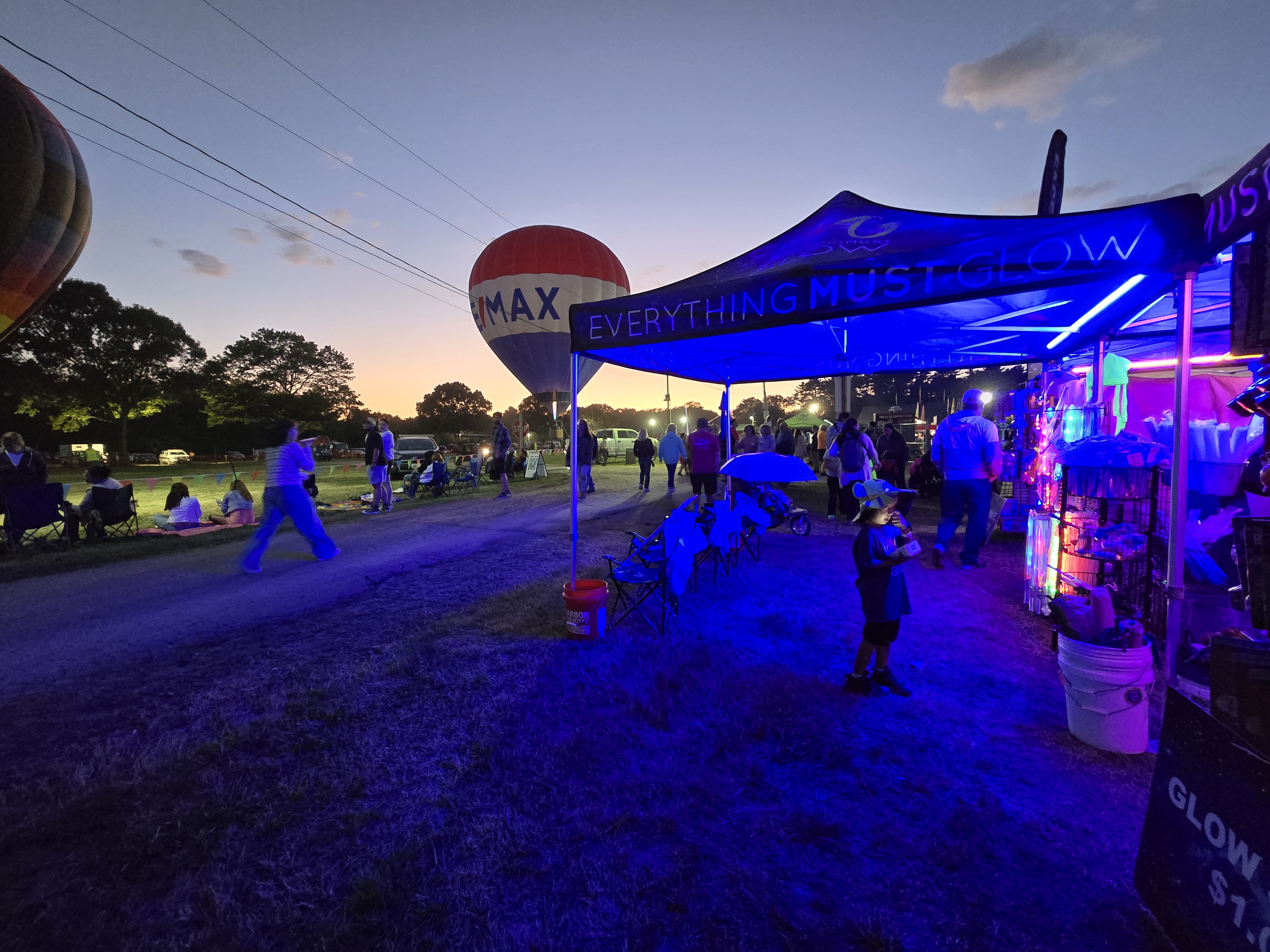 Everything Must Glow booth shining at a balloon glow event at dusk