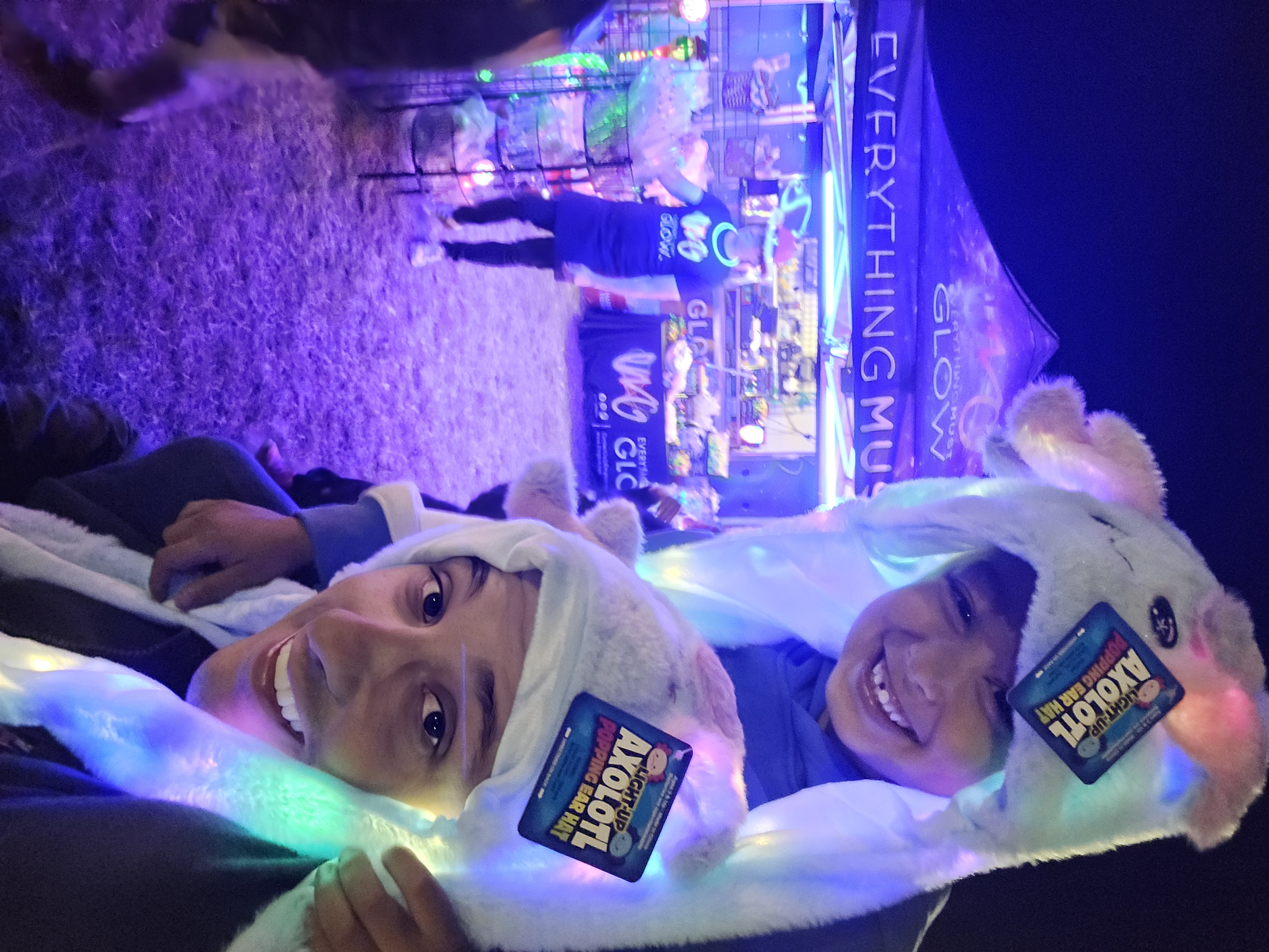 Two smiling kids rocking their light-up axolotl hats at the booth