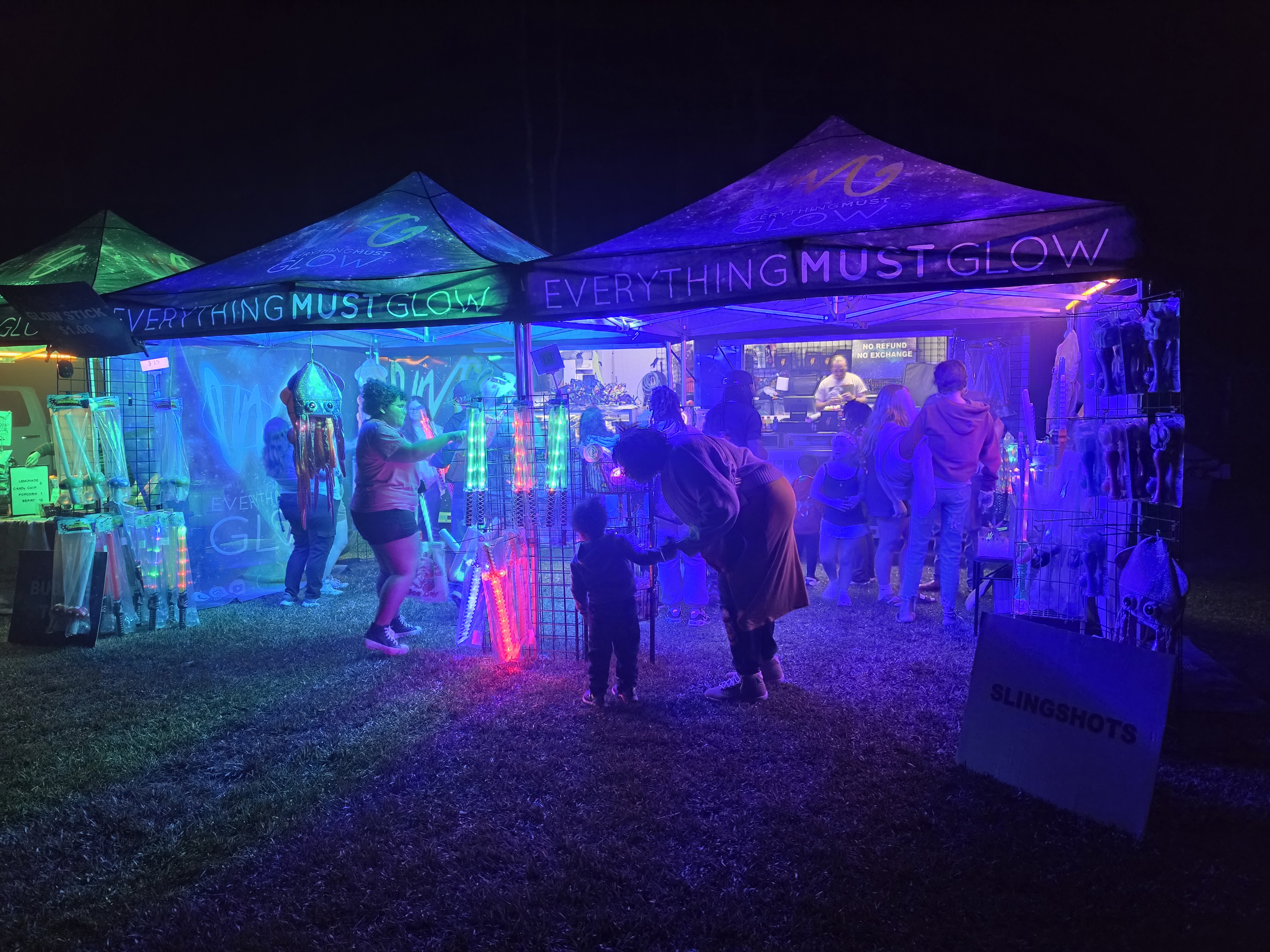 Our double tent booth glowing blue at night with families shopping for glow gear